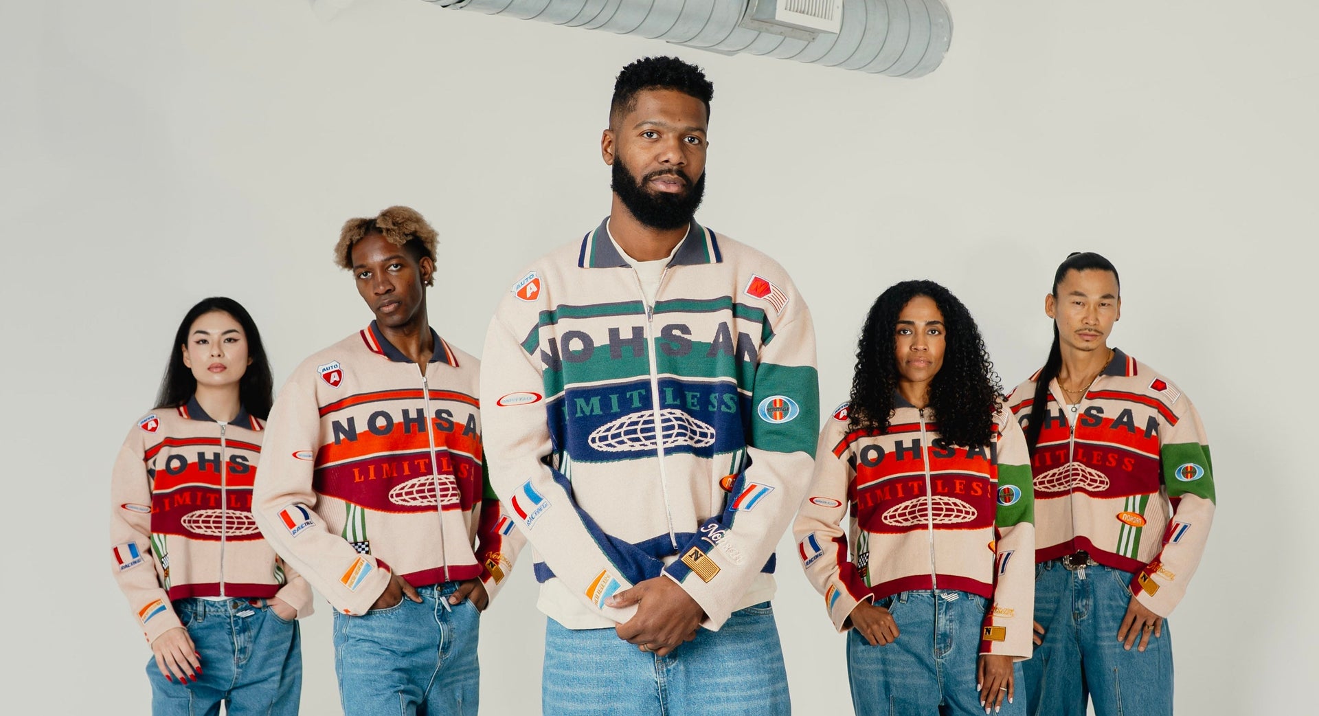 Five people wearing patterned sweaters and jeans standing in a line against a white background.